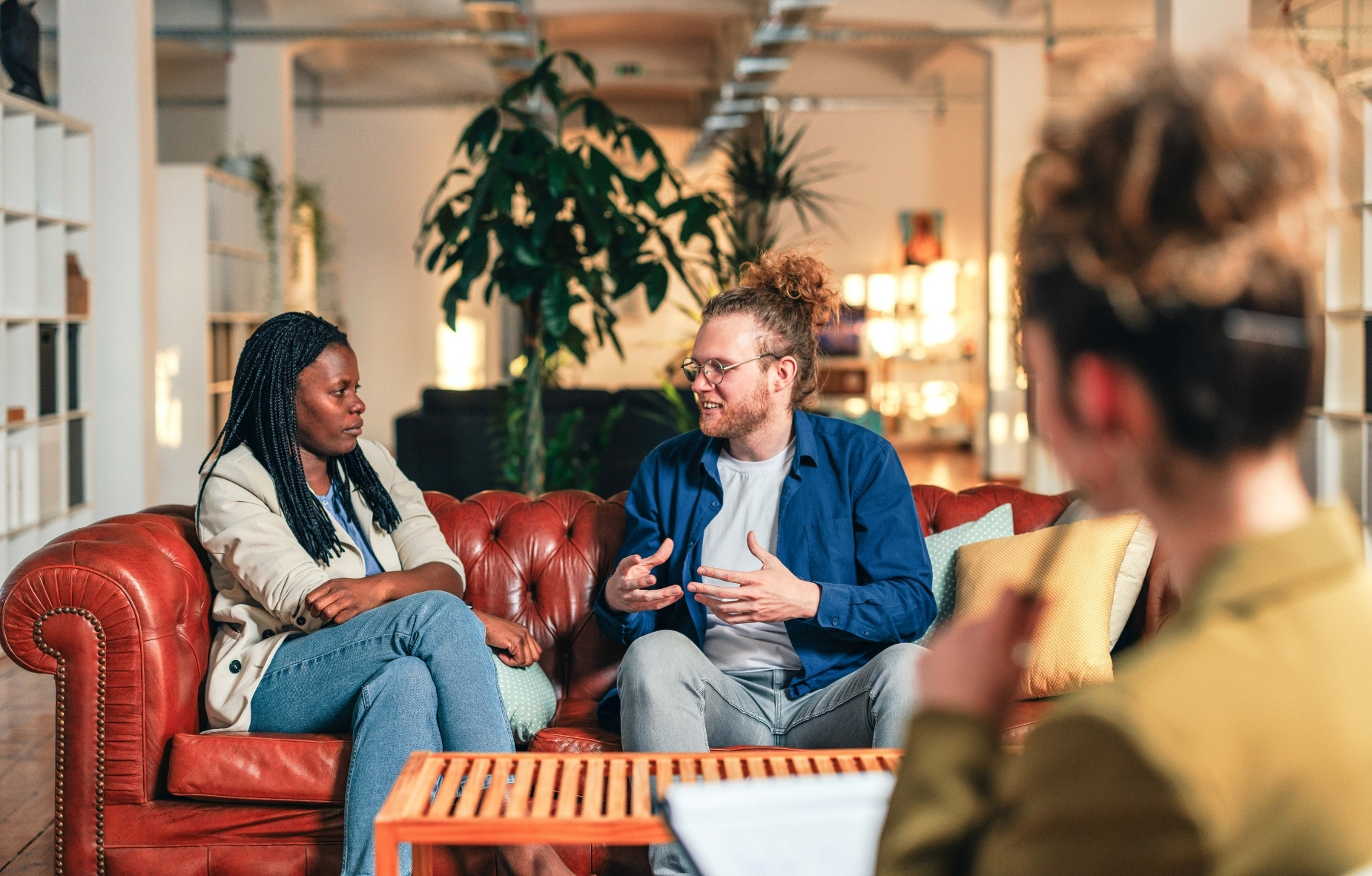 Zwei Personen sitzen auf dem Sofa, eine weitere Person sitzt ihnen gegenüber