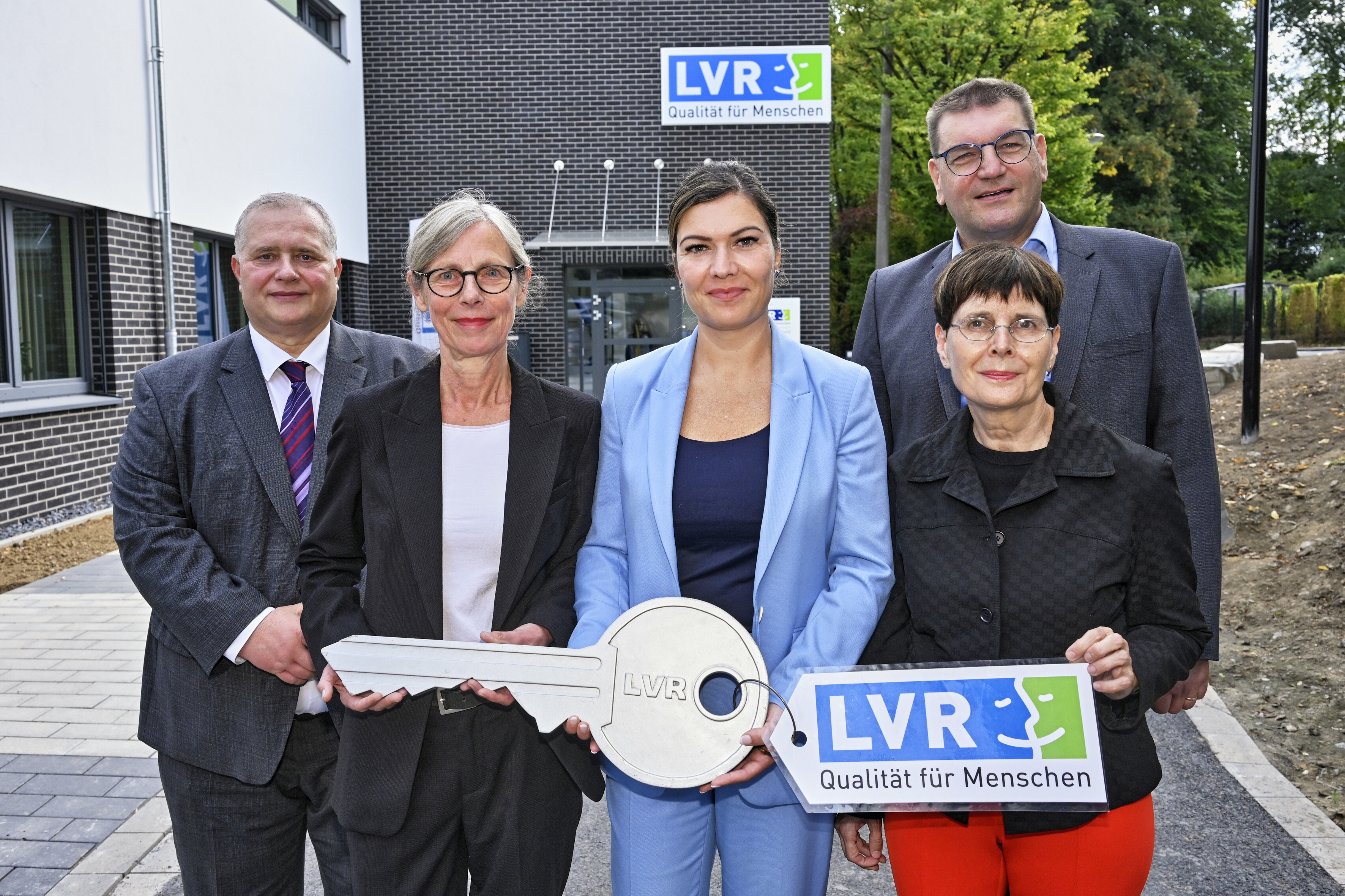 Das Bild zeigt fünf Personen vor einem Gebäude, die einen übergroßen Schlüssel halten.