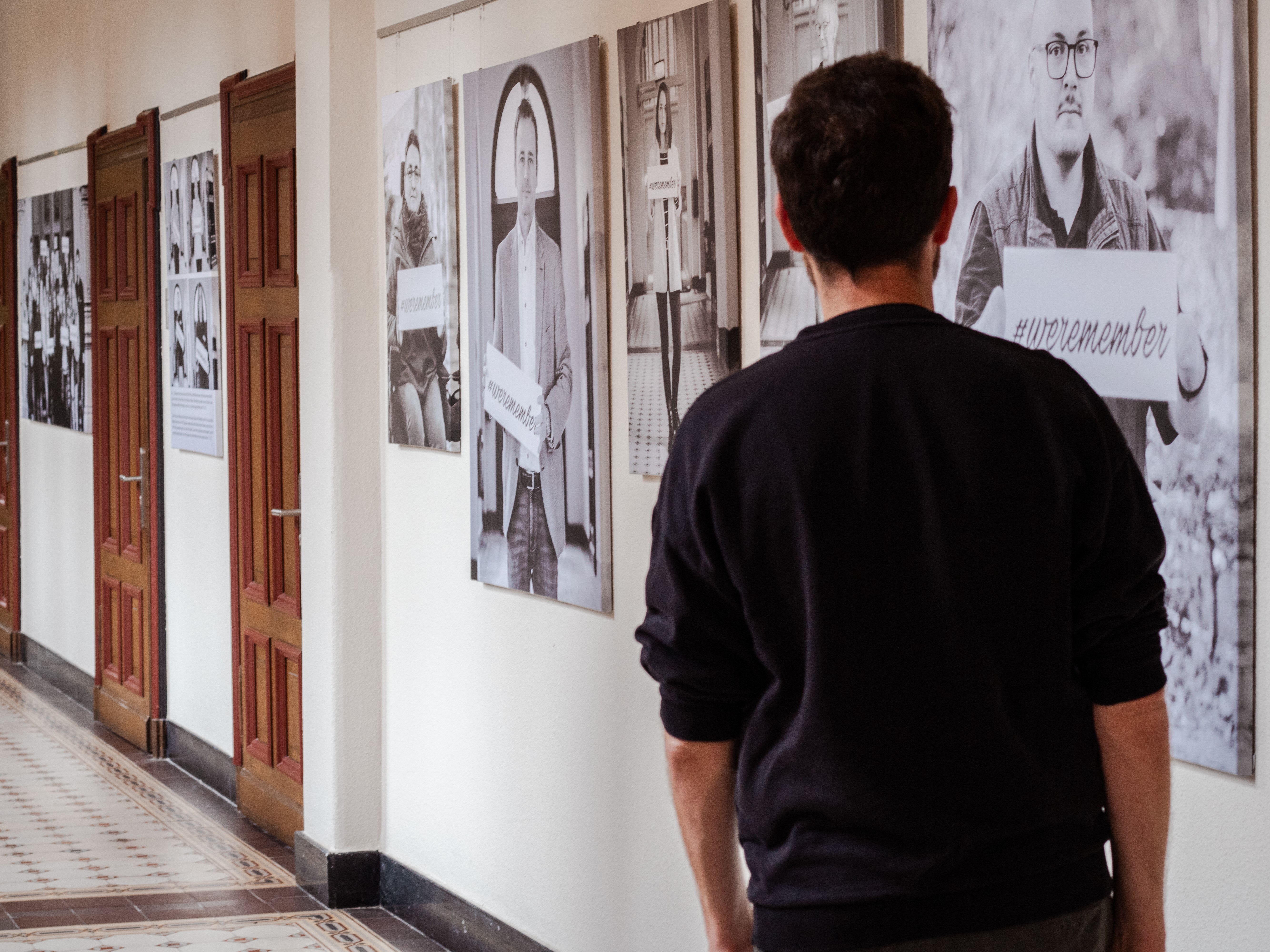 Das Bild zeigt eine Person von hinten, die sich Bilder an einer Wand anschaut.