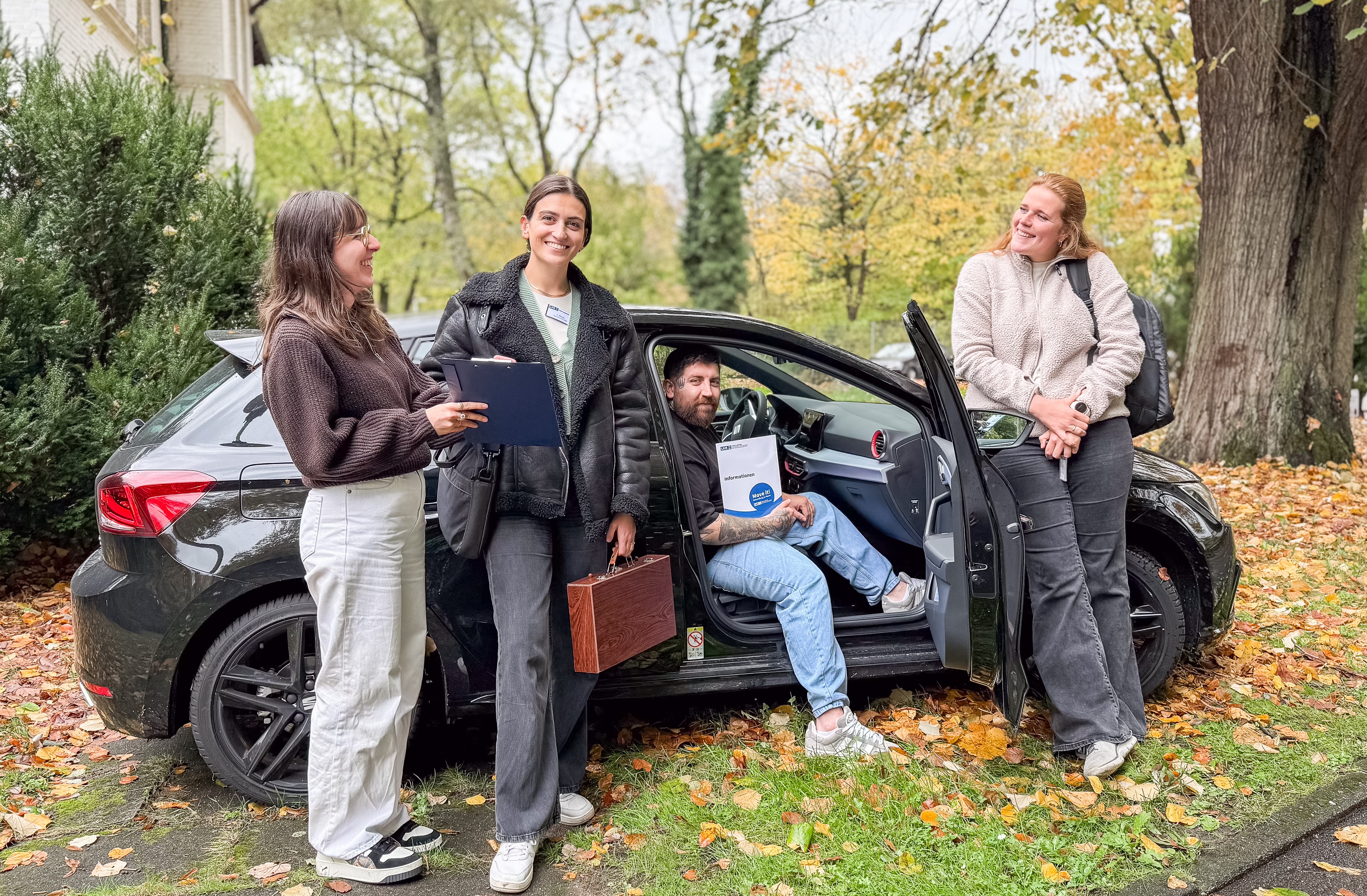 Vier Personen unterhalten sich an einem Auto stehend bzw. sitzend.